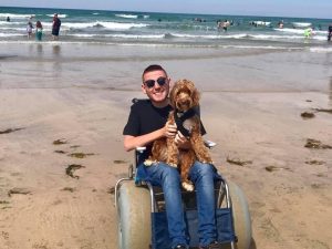 Ross Lannon in a sandchair, with his dog on a beach