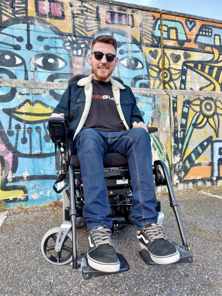 Ross Lannon sitting in his wheelchair with a graffiti wall in the background