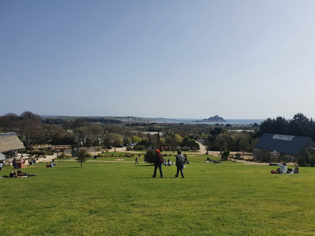 A view from the hill by the cafe looking out towards St. Michael's Mount with people having picnics and stood chatting