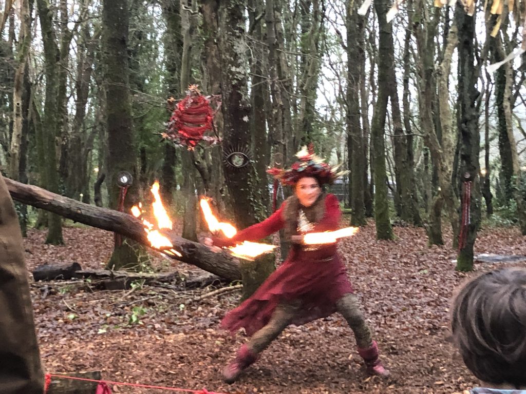 A performer at Rogue Theatre dances with fire sticks in the winter woodland