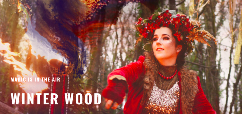 A performer in the woods with red flower garlend around her head and a red robe in the woods surrounded by magical light and the heading Winter Wood in text