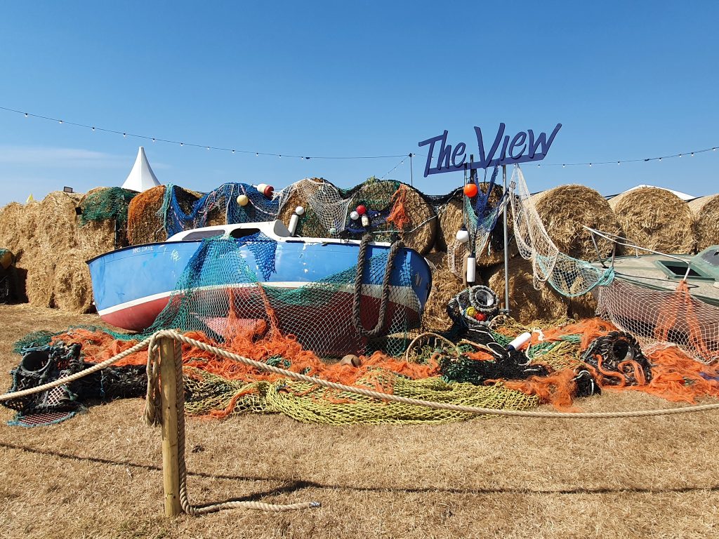 View stage sign and display, a blue boat with lots of orange, green and yellow fishing nets and lobster pots