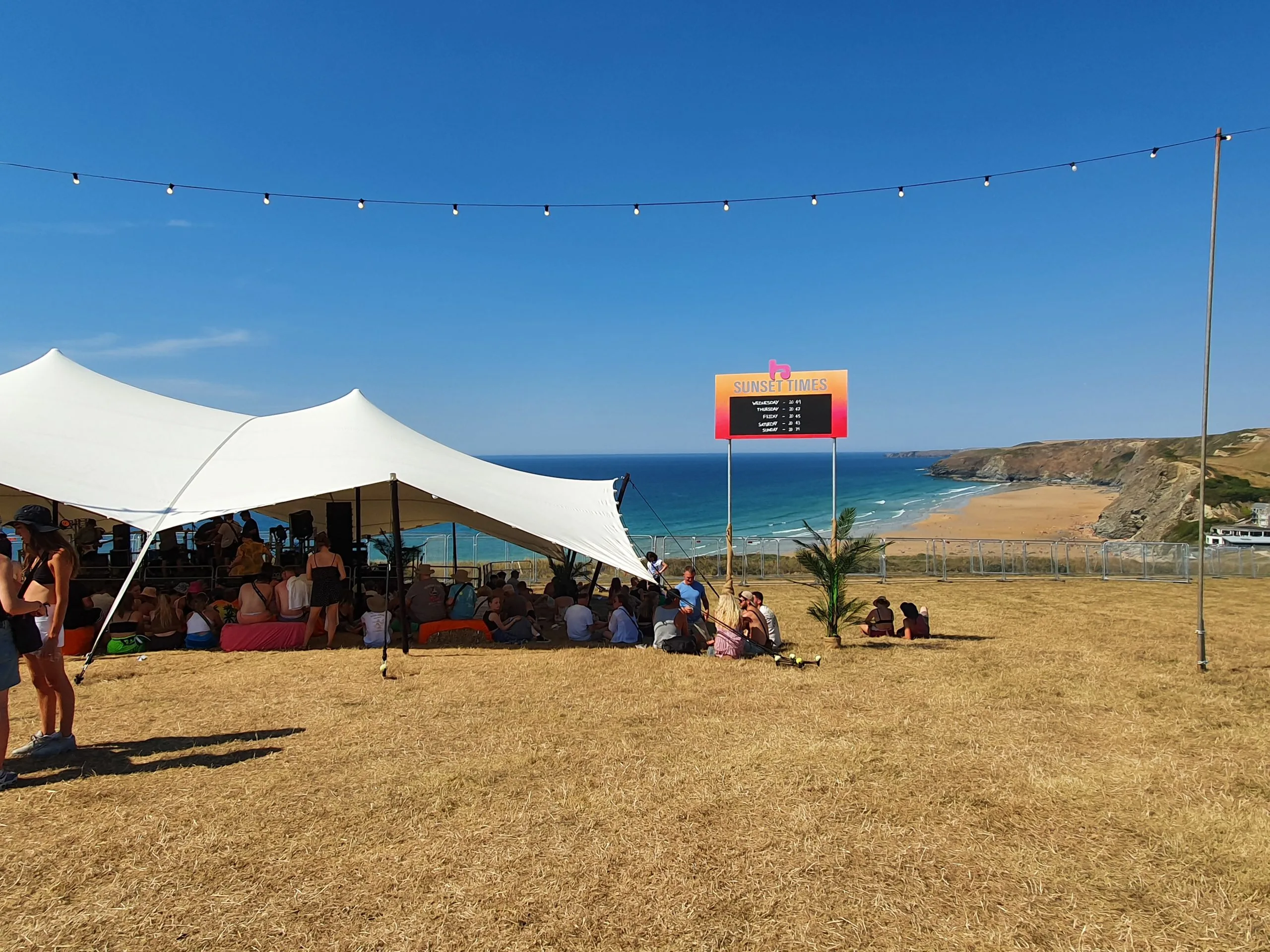 view over watergate bay in newquay, festival tent in the left of the Image and a sign detailing sunset times on the right