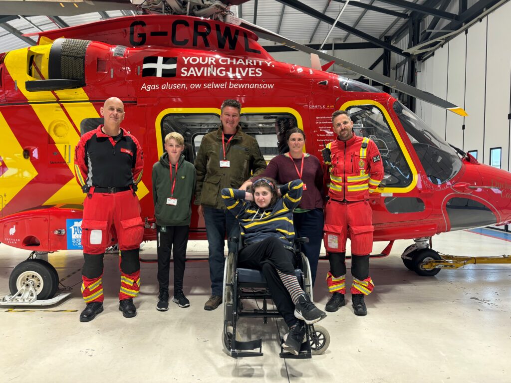 Photo of Holly, family and the air ambulance crew stood in front of the red air ambulance helipcopters