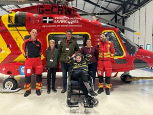 Photo of Holly, family and the air ambulance crew stood in front of the red air ambulance helipcopters