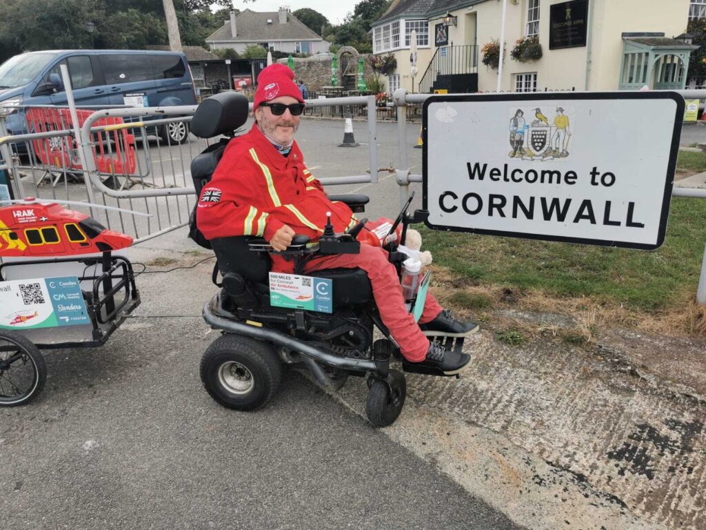 Steven Webb in his wheelchair next to a Welcome to Cornwall sign