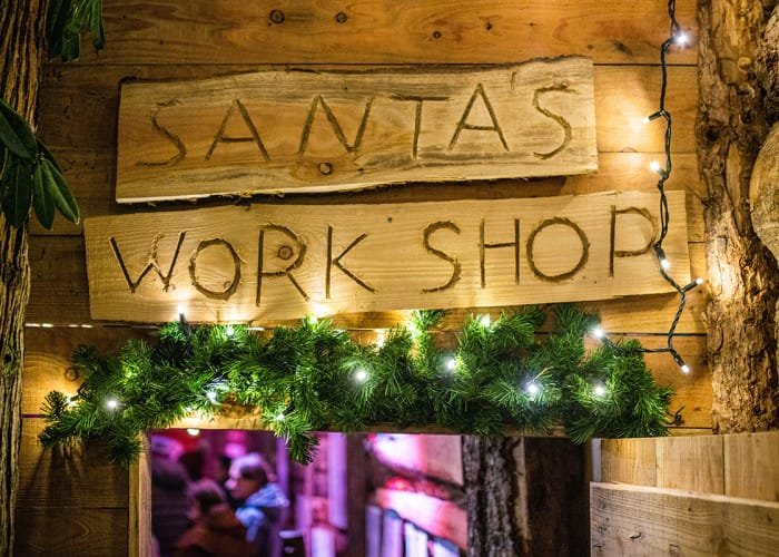 A wooden sign saying Santas Workshop above a doorway 
